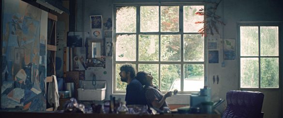 Photo extraite du film : Leïla et Damien assis dos à dos, devant les carreaux d'une fenêtre qui illumine l'intérieur d'un atelier de peintre