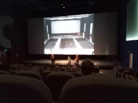 Photo : La salle du Ciné Manivel de Redon ; les participants sont dans la pénombre, trois intervenants se tiennent debout devant la scène éclairée. En fond, la photo d’une salle de cinéma est projetée sur l’écran.