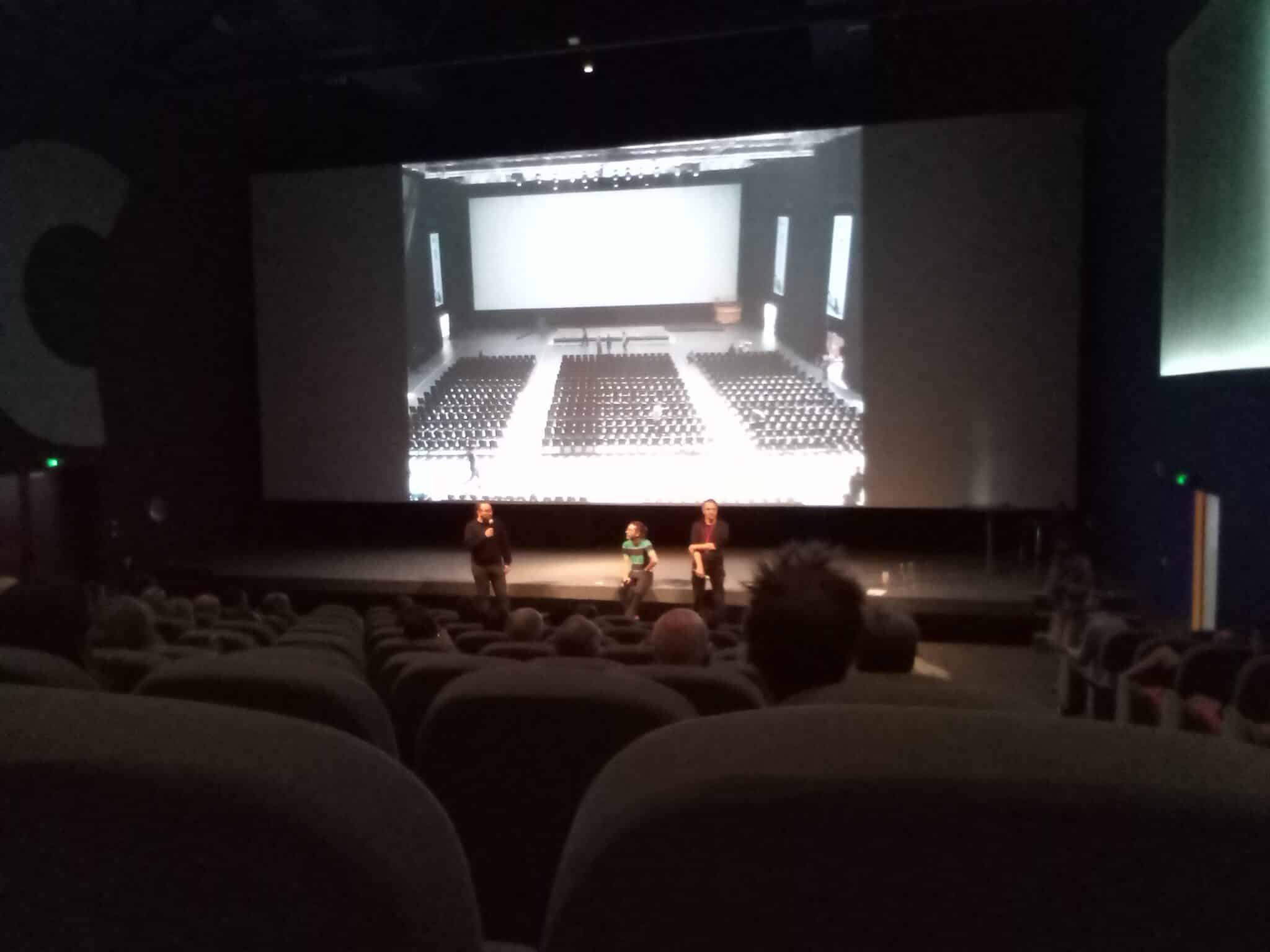 Photo : La salle du Ciné Manivel de Redon ; les participants sont dans la pénombre, trois intervenants se tiennent debout devant la scène éclairée. En fond, la photo d’une salle de cinéma est projetée sur l’écran.