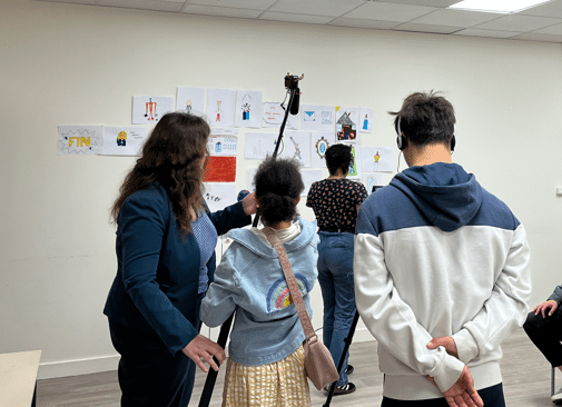 Photo prise lors de l'atelier : 4 jeunes sont de dos. Ils font face à un mur couvert de dessins. L'une d'entre eux tient un microphone à perche.