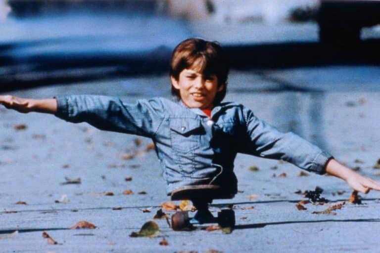 Photo extraite du film Kenny : Un jeune garçon au bas du corps amputé tient en équilibre sur son skateboard, ses bras tendus simulant les ailes d'un avion.