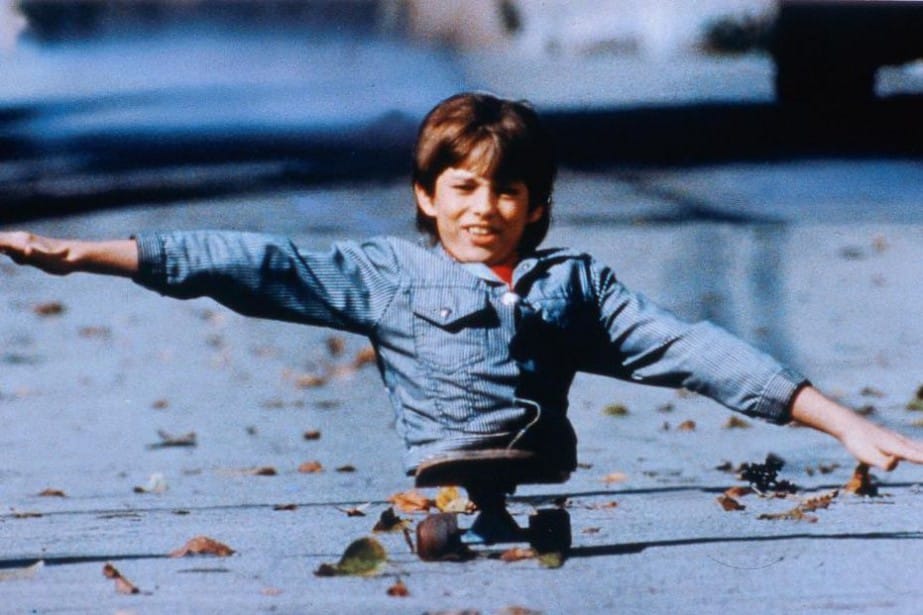 Photo extraite du film Kenny : Un jeune garçon au bas du corps amputé tient en équilibre sur son skateboard, ses bras tendus simulant les ailes d'un avion.