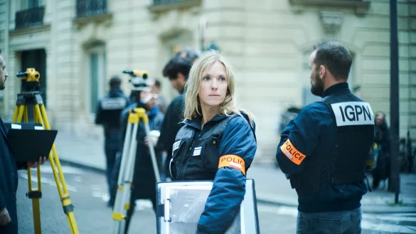 Photo de Dossier 137 : Dans une rue, une femme blonde avec une veste noire et un brassard orange. Elle porte un dossier sous le bras. Un homme se tient de dos à ses côtés. Les lettres IGPN sont inscrites sur sa veste noire, et le mot Police sur les brassards des deux personnes.