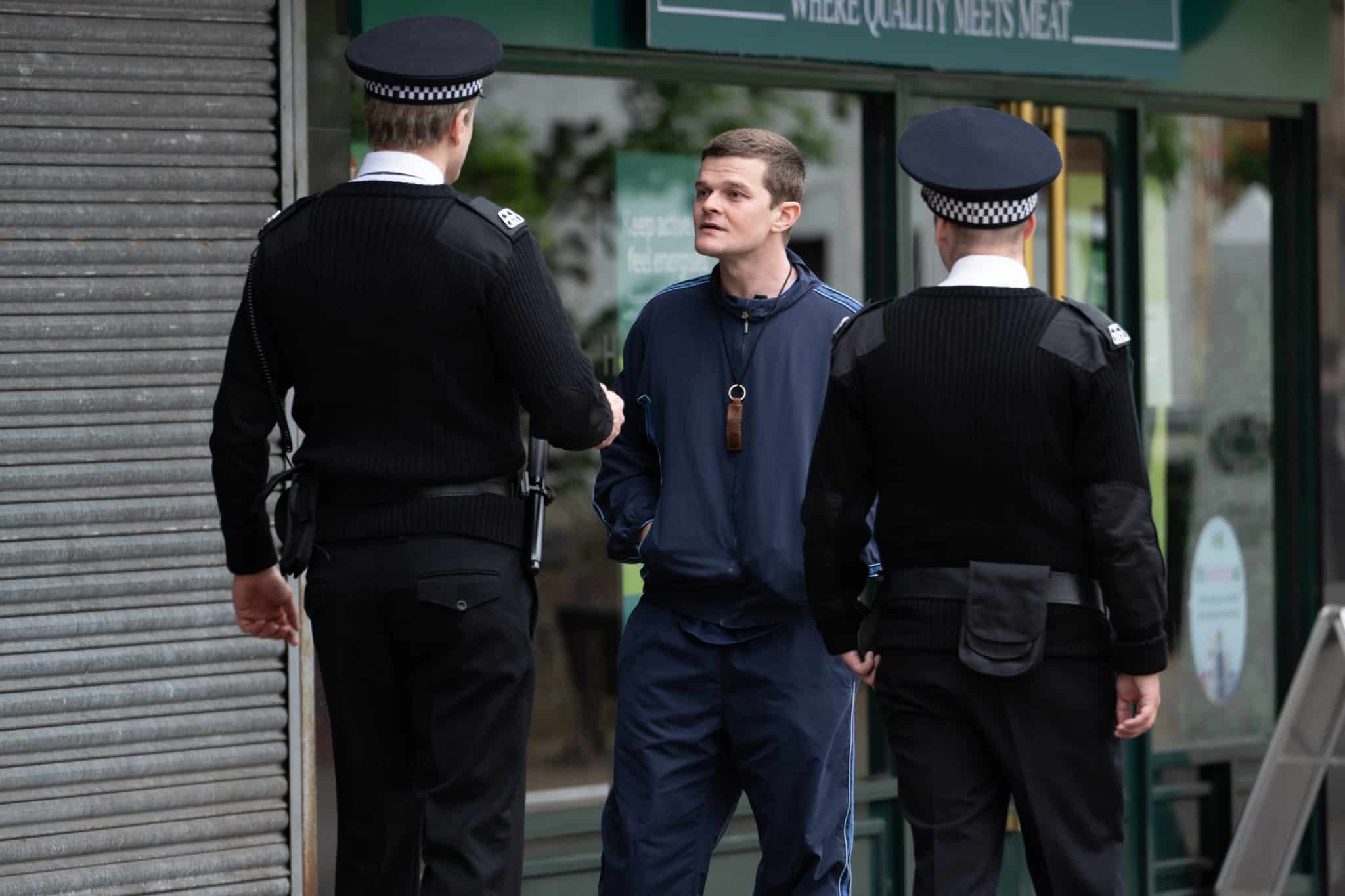 Photo extraite du film Plus fort que moi : De dos, deux hommes avec casquette et uniforme noirs. Face à eux, un jeune homme en jean et veste bleu marine.
