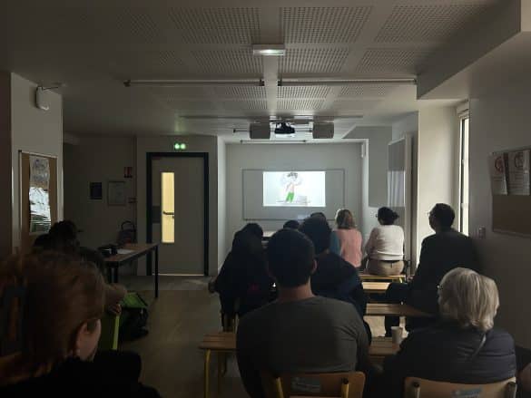 Photo de la restitution au Collège et Lycée Morvan : dans la pénombre, les spectateurs regardent vers l'écran sur lequel est projeté la vidéo des élèves.