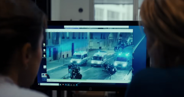 Photo de Dossier 137 : De dos, les profils de deux femmes. Elles regardent un écran d'ordinateur, sur lequel est diffusée une image de rue avec trois camions de CRS.