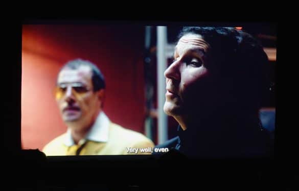 Photo de la projection du film Au-delà du regard au festival ReelAbilities : Sur l'écran de cinéma, le visage d'une femme brune de profil. En second plan, à ses côtés, se tient un homme à lunettes portant une veste jaune. En bas de l'écran, le sous-titre "Very well even" est inscrit.